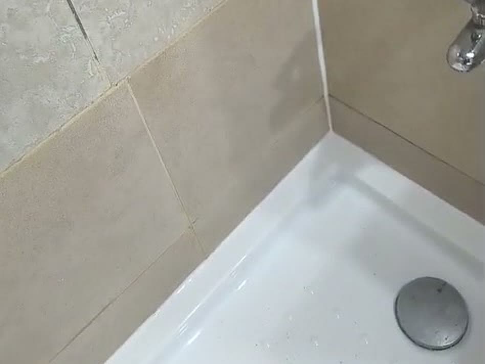 Receptáculo de ducha blanco recién instalado y sellado contra la cerámica, con la llave de la ducha en el muro
