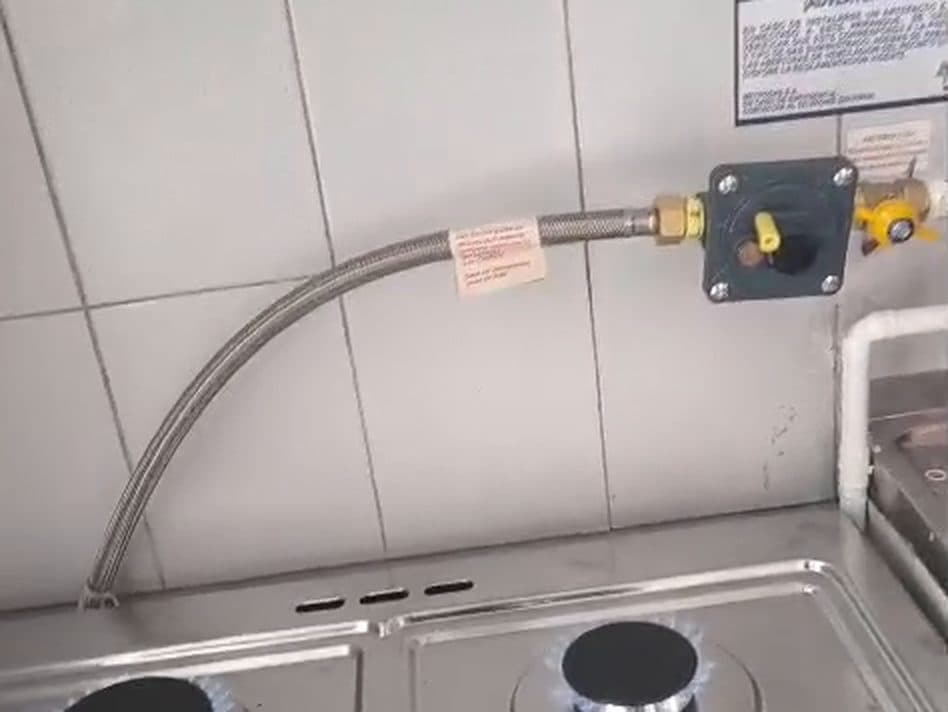 Flexible metálico nuevo entre la llave de paso y una cocina con los quemadores encendidos en llama azul