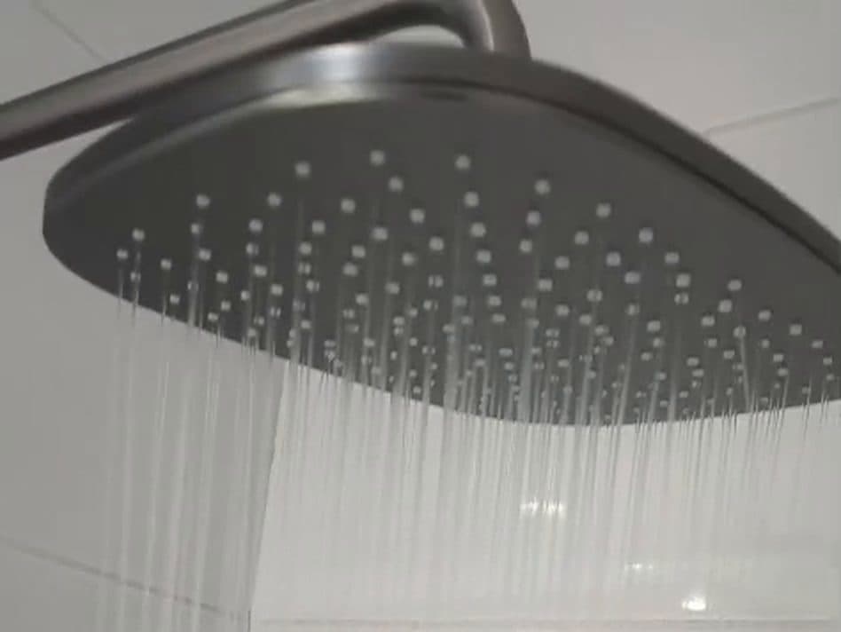 Ducha de lluvia color grafito con el agua corriendo, en un baño de cerámica blanca