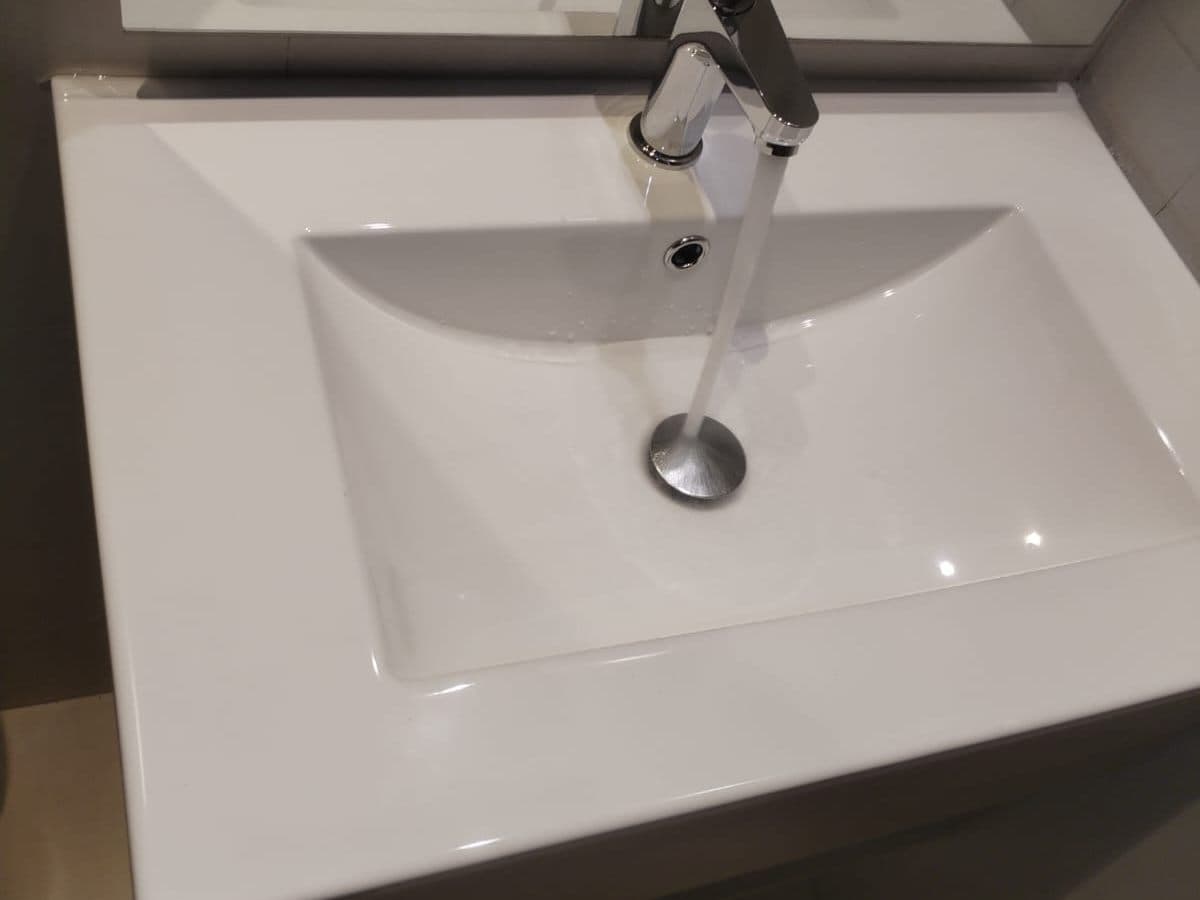 Lavamanos de loza blanca con grifería monomando recién instalado, con el agua corriendo