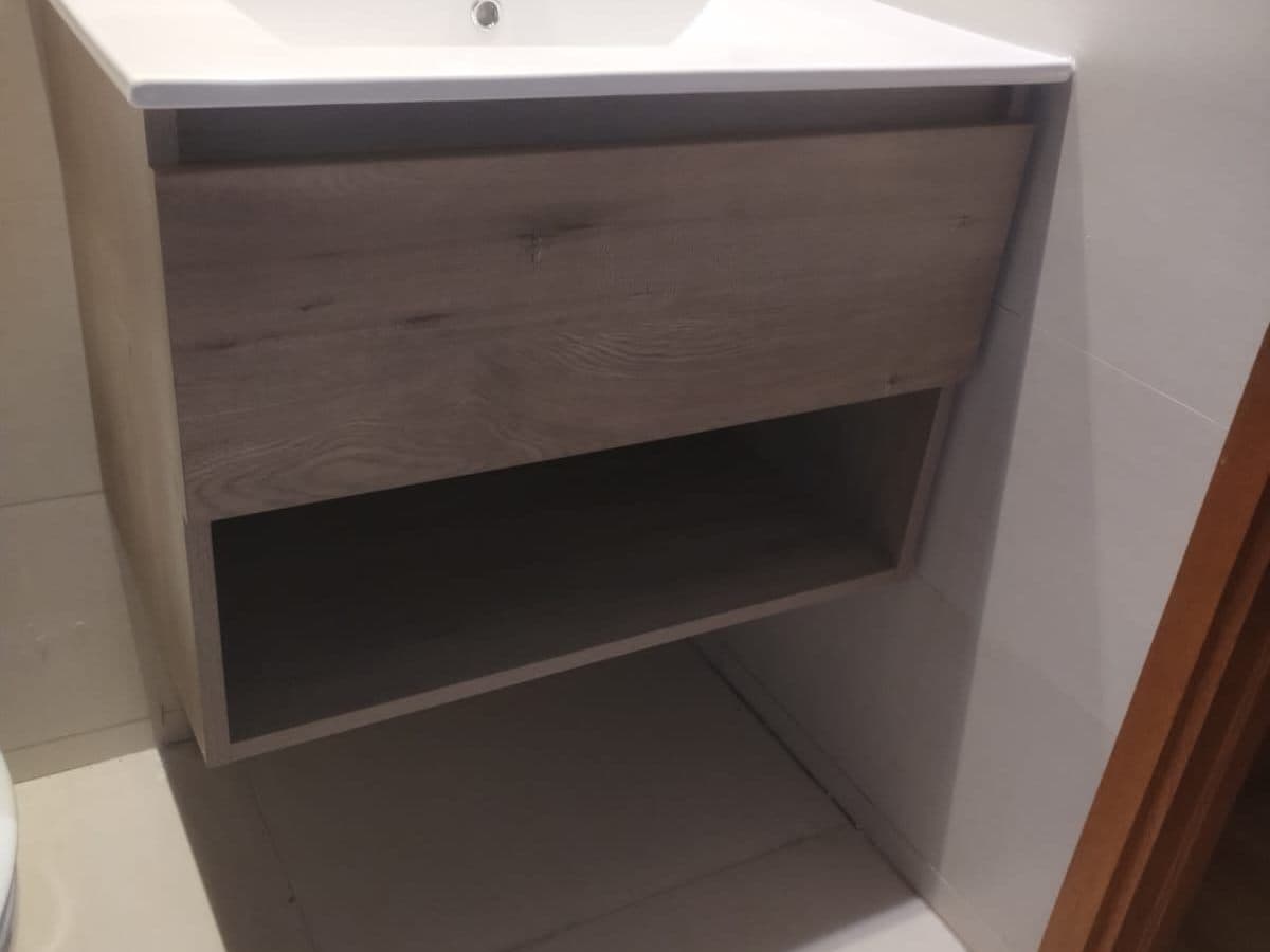 Vanitorio de madera clara con lavamanos de loza instalado en un baño blanco