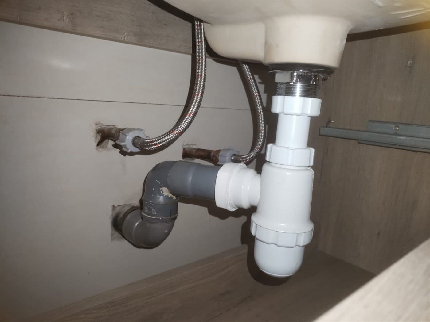 Sifón plástico nuevo instalado bajo un lavamanos, con sus flexibles de agua