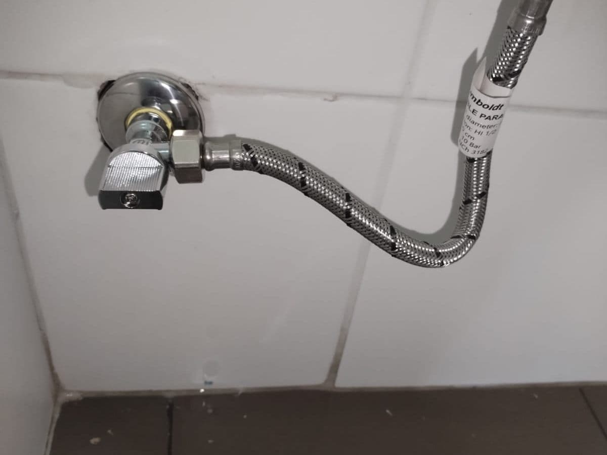 Llave angular y flexible de acero nuevos instalados en un muro de cerámica blanca