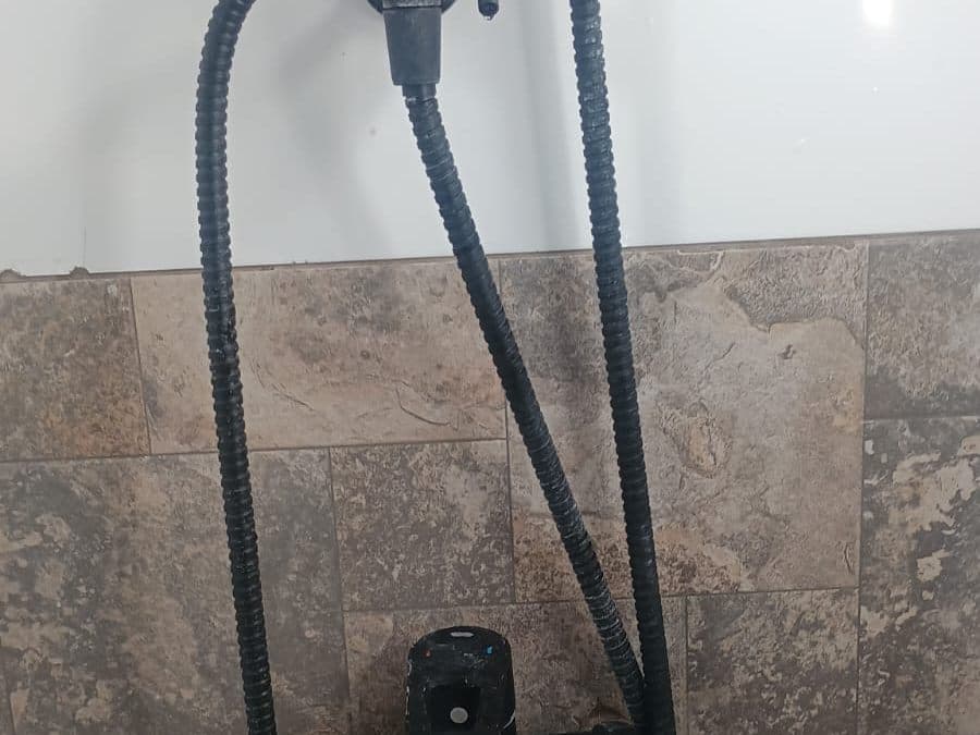 Ducha teléfono negra con su llave instalada sobre un muro de cerámica tipo piedra