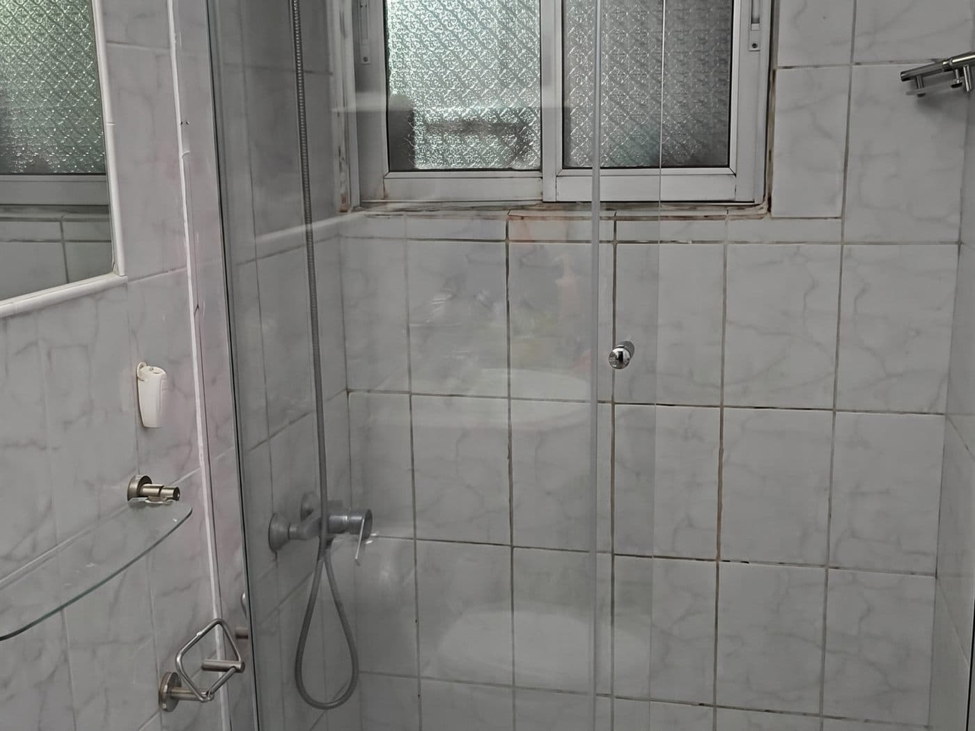 Mampara corredera de vidrio con perfiles cromados instalada en una ducha de cerámica blanca