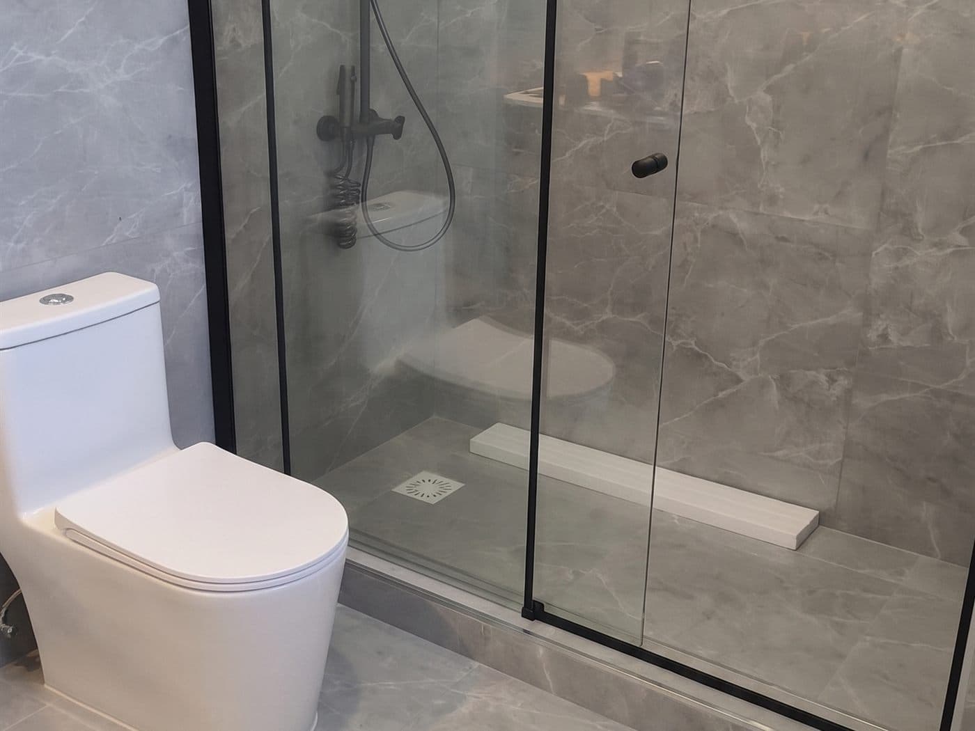 Mampara corredera de vidrio con perfiles negros y columna de ducha en un baño de cerámica gris tipo mármol