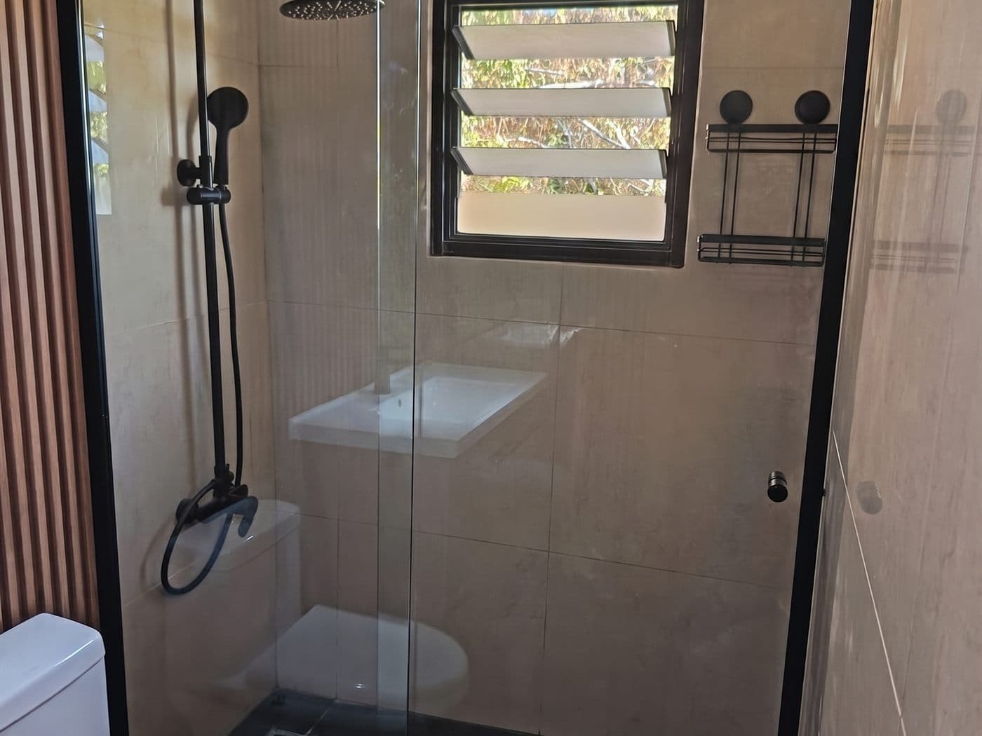 Mampara corredera de vidrio con perfiles negros y ducha negra en un baño de cerámica beige