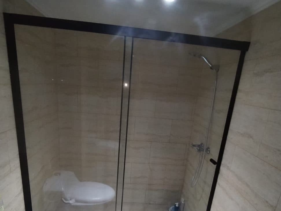 Mampara corredera de vidrio con marco negro cerrando una ducha de cerámica clara