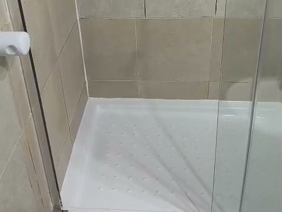 Mampara de vidrio con perfiles cromados sobre un receptáculo de ducha nuevo, en un baño de cerámica beige