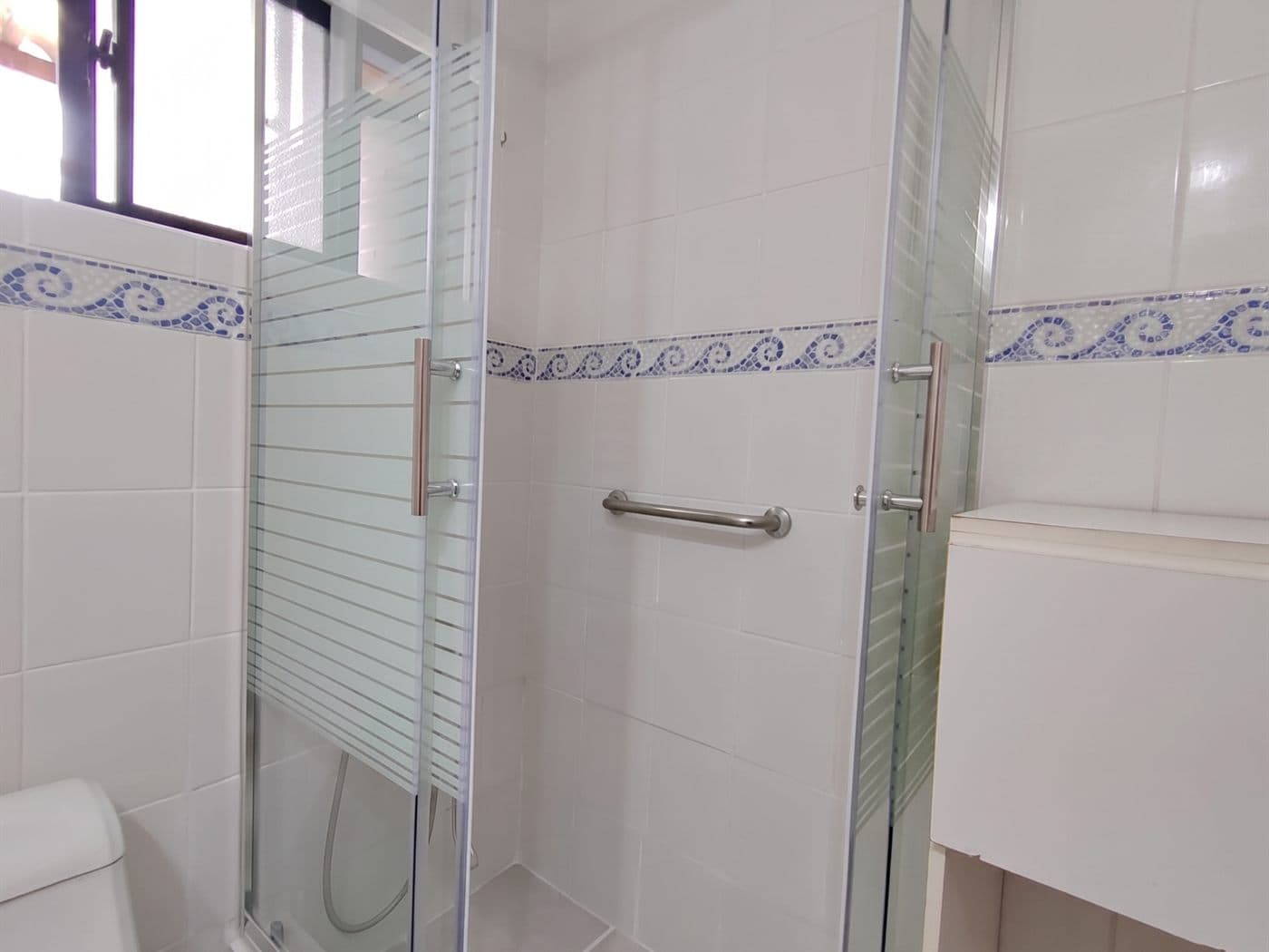 Mampara corredera con franjas satinadas y tiradores cromados en un baño de cerámica blanca